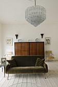 A brown sofa with a chandelier with a Biedermeier cupboard in the background in a room with floor boards