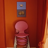 A stack of coloured chairs against an orange wall