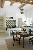 A dining table and a kitchen table in a rustic kitchen in a country house with a wood beam ceiling