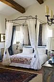 A bedroom in a country house with a metal four poster bed and light curtains