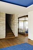 An anteroom with walnut floor boards and a wooden staircase built into a natural stone wall and a view of a window