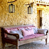 A Mediterranean country house - a rustic bench with checked upholstery and lanterns hanging on the exterior, natural stone walls