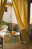 A balcony overlooking the courtyard of an apartment block with a curtain - wicker chairs and refreshments on a tray