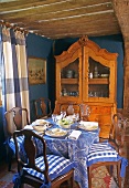 Essen im Bauernhaus - antike Vitrine vor blauer Wand und Holzbalkendecke