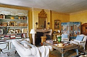 A yellow-painted living room in a country house with a sofa and a and coffee table in front of a fireplace