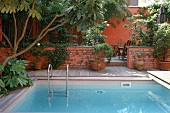 Pool mit Leiter vor rotgetünchter Steinmauer in einer Hausanlage