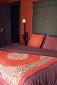 A bed with an oriental throw and a brick red wall