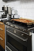A baked pizza on a stainless steel gas cooker against a white wall