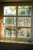 Stillleben auf Fensterbank - alte Flaschen und Vasen mit Blumen vor Sprossenfenster