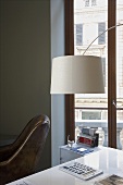 A white lampshade above a table and a window with a view