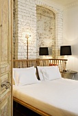 A view through an open door onto a double bed with a wooden slatted head rest against a white painted brick wall