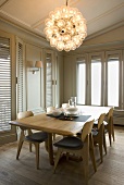 50s style wooden dining table and designer hanging light in the corner of a living room with bright gray wood paneling