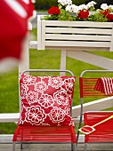 Garden chairs with red fabric covering and pillows in front of a railing with window boxes