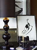 Tischlampe mit schwarzem Schirm und Fuss neben Kamera und gerahmten Bild