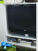 TV in a white bookcase and upholstered stool with stuffed animal