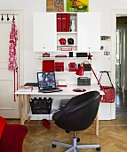 A black swivel chair in front of a white desk and a wall-mounted cabinet with a self