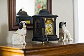 Antique clock and ceramic dog figurines in front of a framed mirror