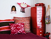 Kinderzimmerecke mit bunten Kissen auf Bett und rotem Metallcontainer mit Schubladen