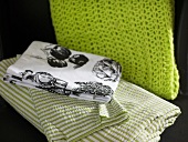 Tischdecke mit ländlichen Motiven und gestreifte Bettwäsche neben grünem Strickschal