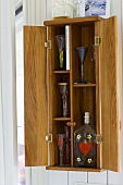 Wooden wall cupboard with open doors and view of stemware and glass bottles inside