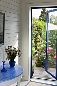 A curved metal wall table with a blue top and a view through an open door into the garden