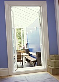 Blauer Flur mit offener Tür und Blick in Wintergarten auf Tisch und Bank