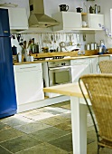 A detail of a modern kitchen diner with white units, stainless steel integral oven, table, cane chairs