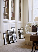 A detail of a traditional, neutral sitting room, built in bookcases, collection of framed photographs leaning against cupboard, natural flooring