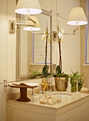 A detail of a traditional bathroom, showing a wash basin set in a unit, mirror, wall lights, gold mirror