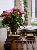 A detail of a modern dining table, Japanese bowls, chopsticks, arrangement of pink roses in glass vase