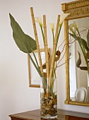Plant leaves and bamboo with lilies in glass vase