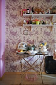Vintage Metalltisch mit Geschirr und Konsolen vor Tapete an Wand mit Blumenmuster