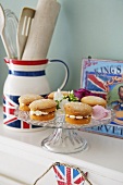 Fairy cakes on a glass cake stand and kitchen utensils in a Union Jack flag jug