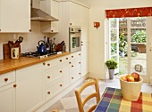 Küche mit weißen Schrankfronten und kugelförmigen Holzgriffen und Gartentür