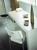 Schlichter Tisch mit Dekoschalen im Fifties Stil und weißer Plastikstuhl vor Fenster
