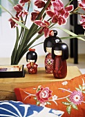 Bemalte Puppen in japanischem Stil neben Orchideen und bestickten Kissen