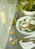 Small rounds of cheese on white plates, lit candles on table