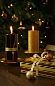 Burning candles with shiny and matte gold surfaces next to Christmas gifts