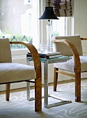 A detail of a modern sitting room showing wooden upholstered armchairs, nest of chrome side tables, lamp