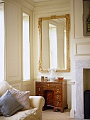 Sitting room with white panelled walls and gilt mirror above antique knee hole desk.