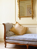 Backless sofa under gilt mirror in sitting room with white panelled walls.