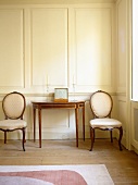 Side table and matching pair of cushioned chairs in dining room with panelled walls.