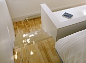 A detail of steps from a modern bedroom to an office area, wooden flooring, white walls,