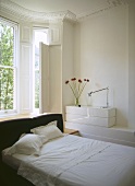 A modern bedroom in neutral colours, a double bed with upholstered headboard, bed linen, bay window with shutters, traditional room with period detail