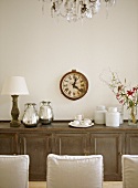 A detail of a traditional, neutral dining room with a wood sideboard, upholstered chairs, modern ceramic pieces