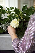 A white rose being held in front of a flower arrangement