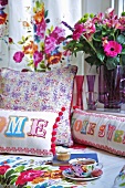 A tea break on a bed with colourful cushions and a bunch of flowers
