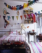 A child's bedroom with a white-painted brass bed and a garland hanging from the ceiling