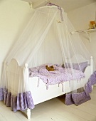 A child's bed with a white, wooden frame and a canopy