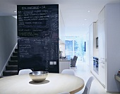 A dining room in an open-plan living room-cum-kitchen and a floor-to-ceiling blackboard next to a flight of stairs